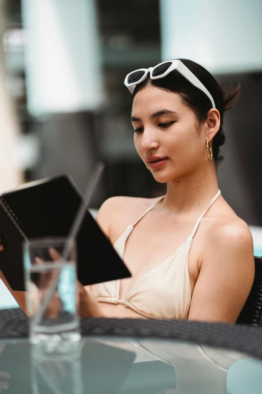 a woman sitting at a table reading a book, trending on pexels, renaissance, is wearing a swimsuit, dua lipa, headshot, drink