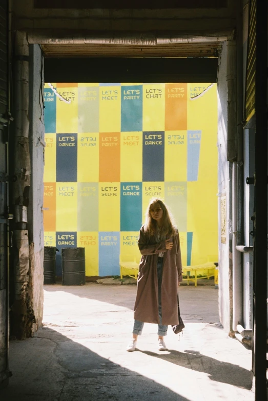 a woman is walking through an open door, poster art, inspired by Elsa Bleda, unsplash, graffiti, long yellow hair, light brown trenchcoat, festivals, in front of a garage