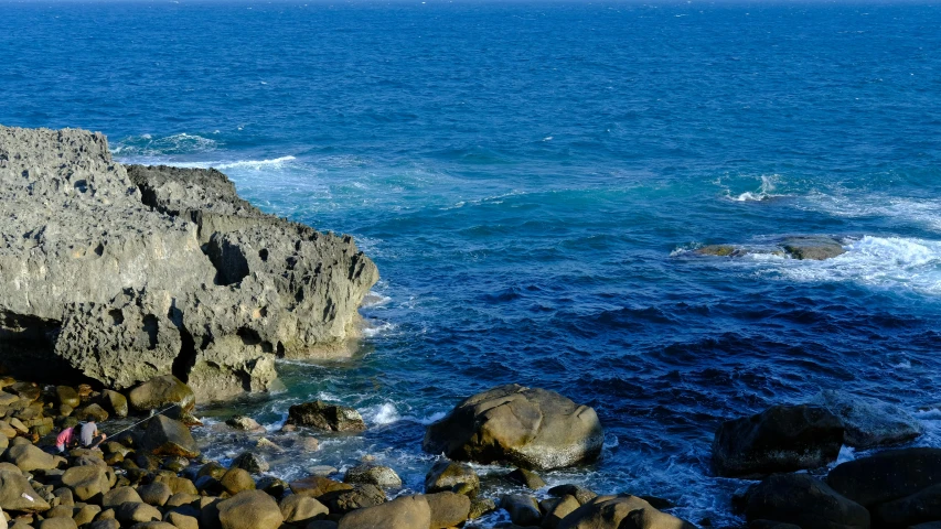 a group of people standing on top of a rocky beach, deep blue ocean color, picton blue, pch, rocks