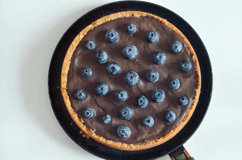 a close up of a pie in a pan on a table, wearing a blue berries, chocolate river, detailed product image, full frontal shot