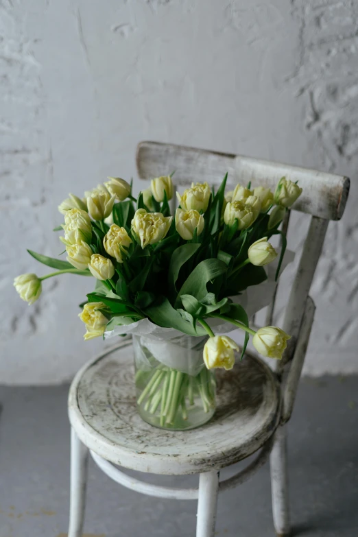 a vase filled with yellow flowers sitting on a chair, inspired by Cy Twombly, romanticism, tulip, with a white, rustic