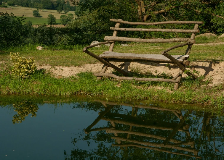 a wooden bench sitting next to a body of water, inspired by Otakar Sedloň, land art, in the countryside, reflections, not cropped, delightful surroundings