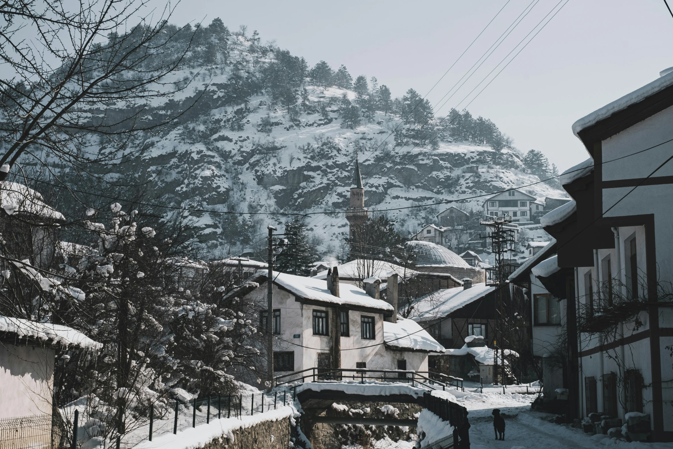 a person walking down a snow covered street, pexels contest winner, hurufiyya, the village on the cliff, bosnian, grayish, thumbnail