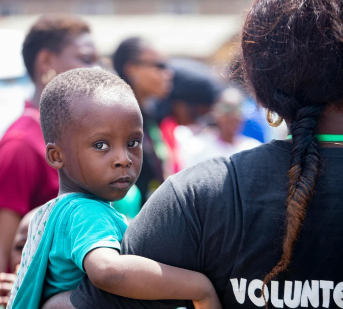 a woman holding a child in her arms, a photo, by Daniel Lieske, pexels contest winner, hurufiyya, community celebration, very kenyan, back towards camera, thumbnail