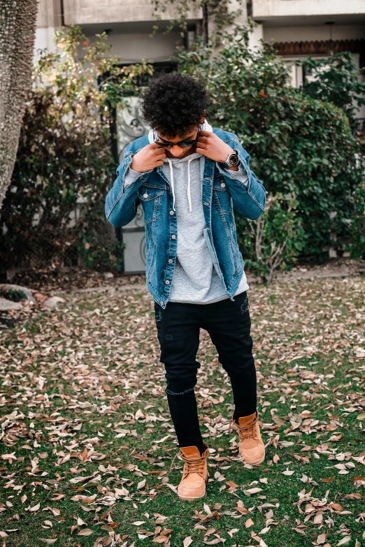 a man standing on top of a lush green field, an album cover, by Robbie Trevino, trending on pexels, realism, wearing a jeans jackets, street wear, profile image, winter vibes