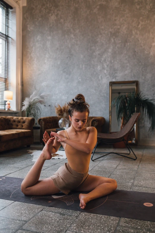 a woman sitting on a yoga mat in a living room, by Matija Jama, unsplash contest winner, arabesque, sexy pose, square, pixeled stretching, brown