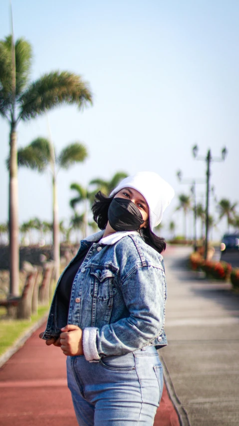 a woman riding a skateboard down a sidewalk, an album cover, unsplash, balaclava mask, palm trees in the background, wearing a jeans jackets, while smiling for a photograph