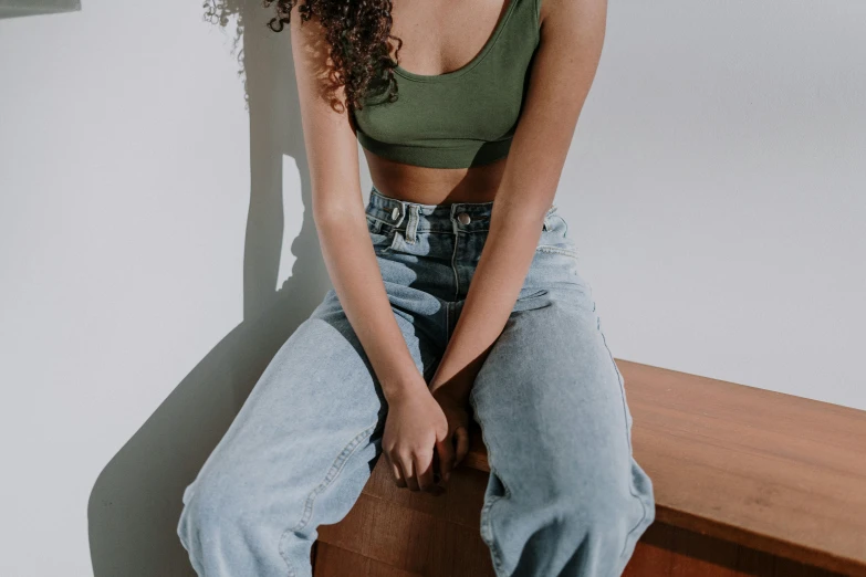 a woman sitting on top of a wooden bench, trending on pexels, wearing crop top, baggy jeans, wearing green clothing, on a white table