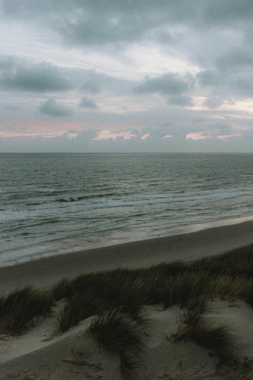 a man standing on top of a sandy beach next to the ocean, by Jan Tengnagel, happening, overcast dusk, dunes, panorama, 8 k -