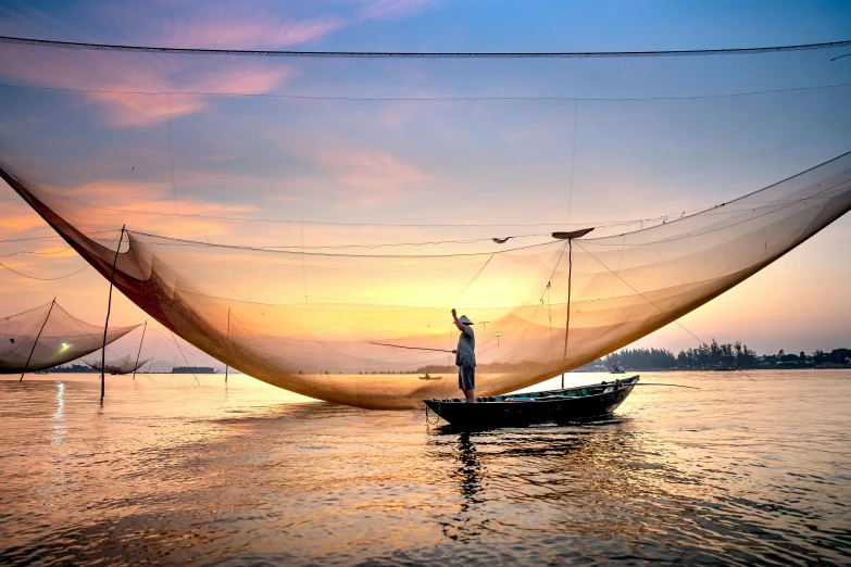 a man standing on top of a boat next to a net, inspired by Steve McCurry, pexels contest winner, warm glow, phuoc quan, wide angle river, skies behind