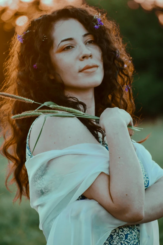 a woman standing in a field holding a bunch of flowers, inspired by Elsa Bleda, renaissance, brown curly hair, promo photo, portrait image, concert