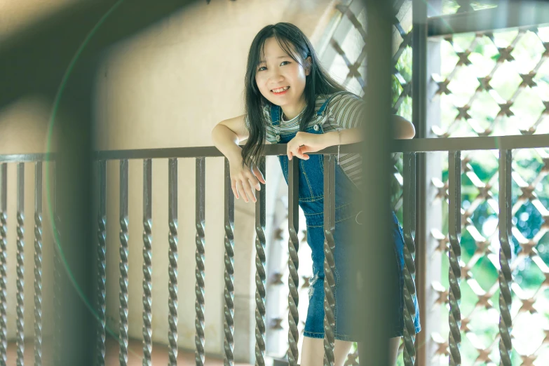 a woman standing on top of a balcony next to a fence, a picture, inspired by Kim Jeong-hui, pexels contest winner, young cute wan asian face, medium format. soft light, indoor picture, wearing overalls
