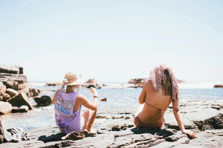 a couple of women sitting on top of a rocky beach, trending on pexels, purple mullet, on a hot australian day, sunburn, college girls