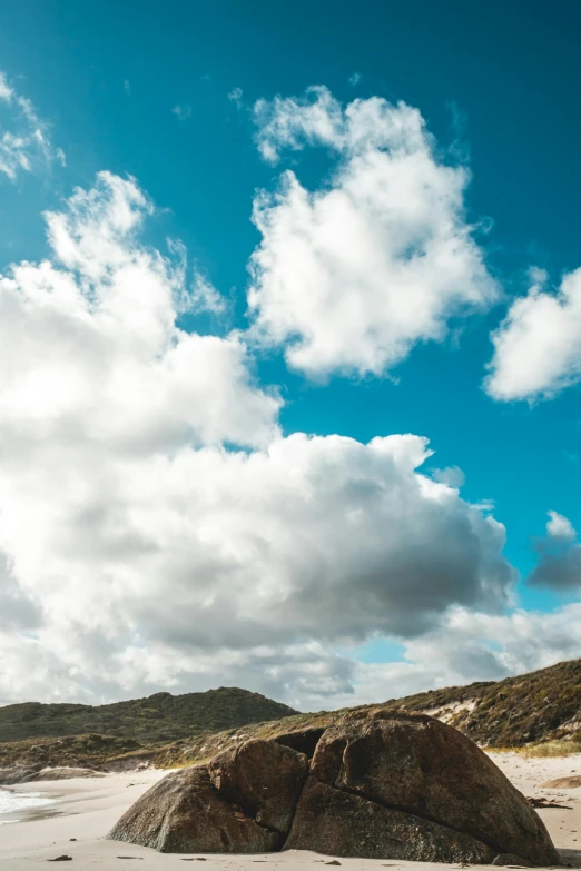 a large rock sitting on top of a sandy beach, giant clouds, sky blue, wellington, sky - high view