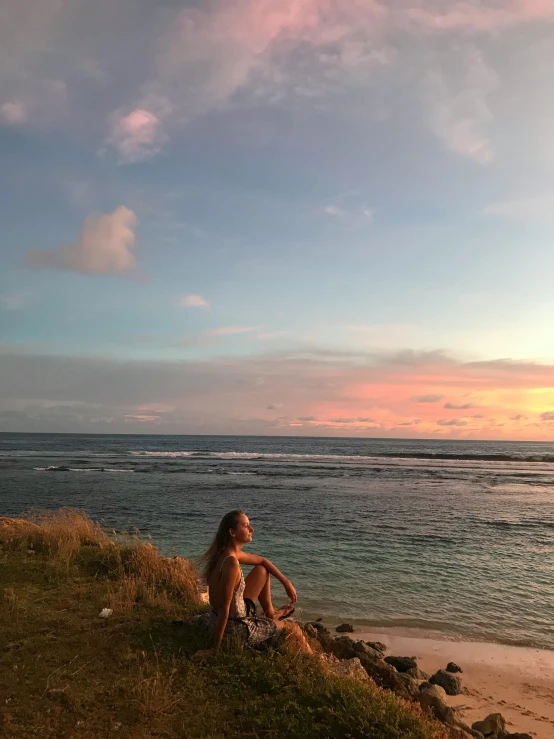 a woman sitting on top of a hill next to the ocean, sunset beach, profile image