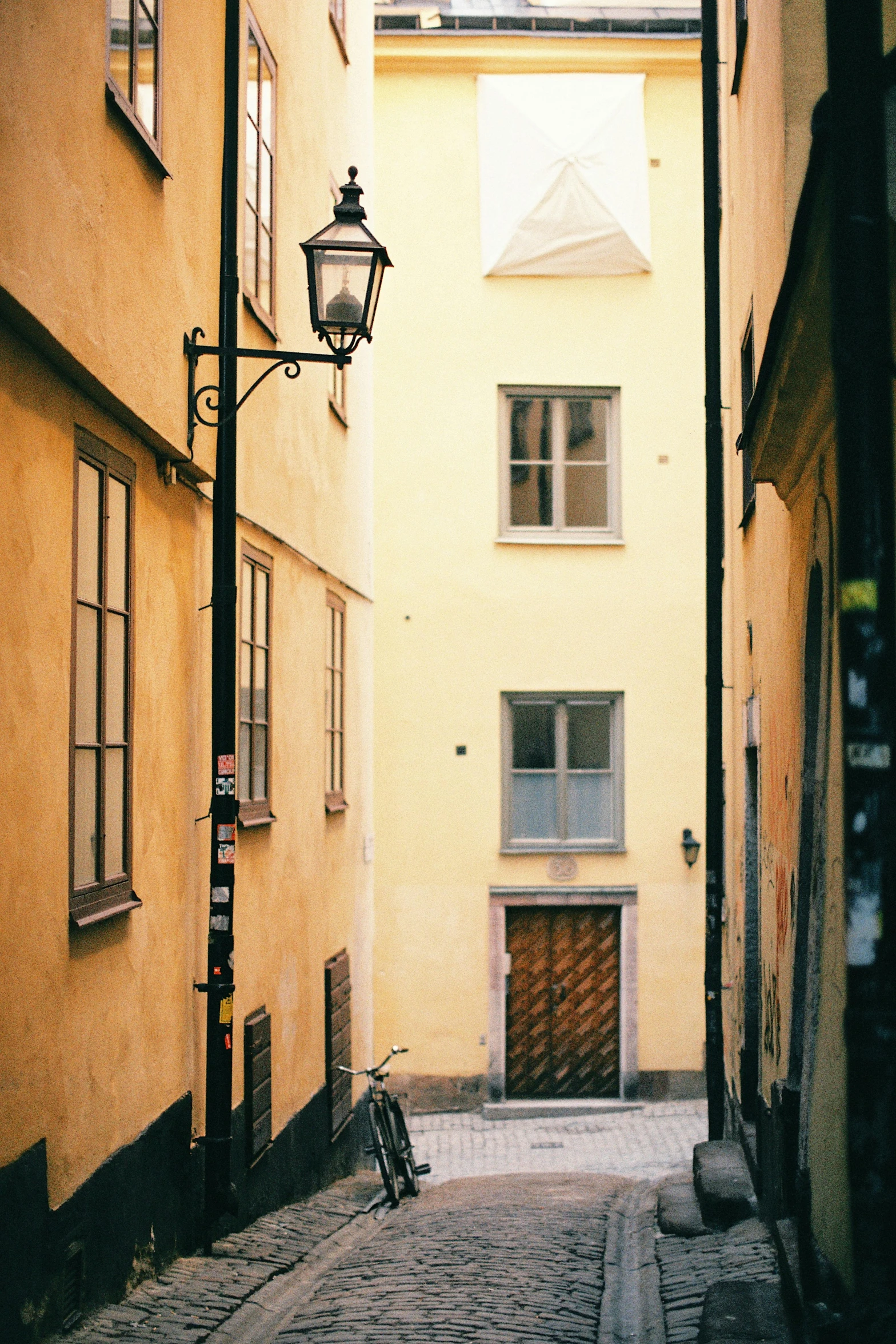 a bicycle is parked on a cobblestone street, inspired by Carl Gustaf Pilo, pale yellow walls, golden windows, street lanterns, colour photograph
