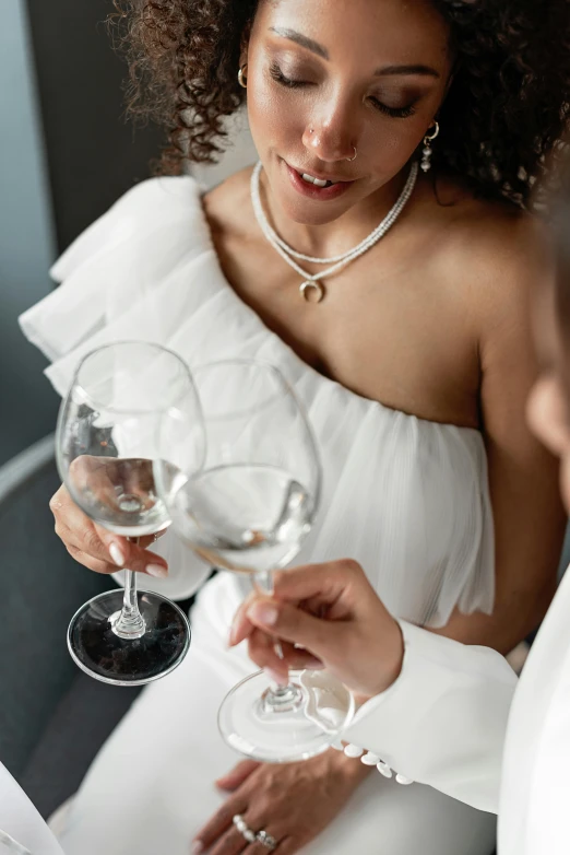 a woman in a white dress holding a glass of wine, hints of silver jewelry, wearing white v - neck top, private moment, glassware