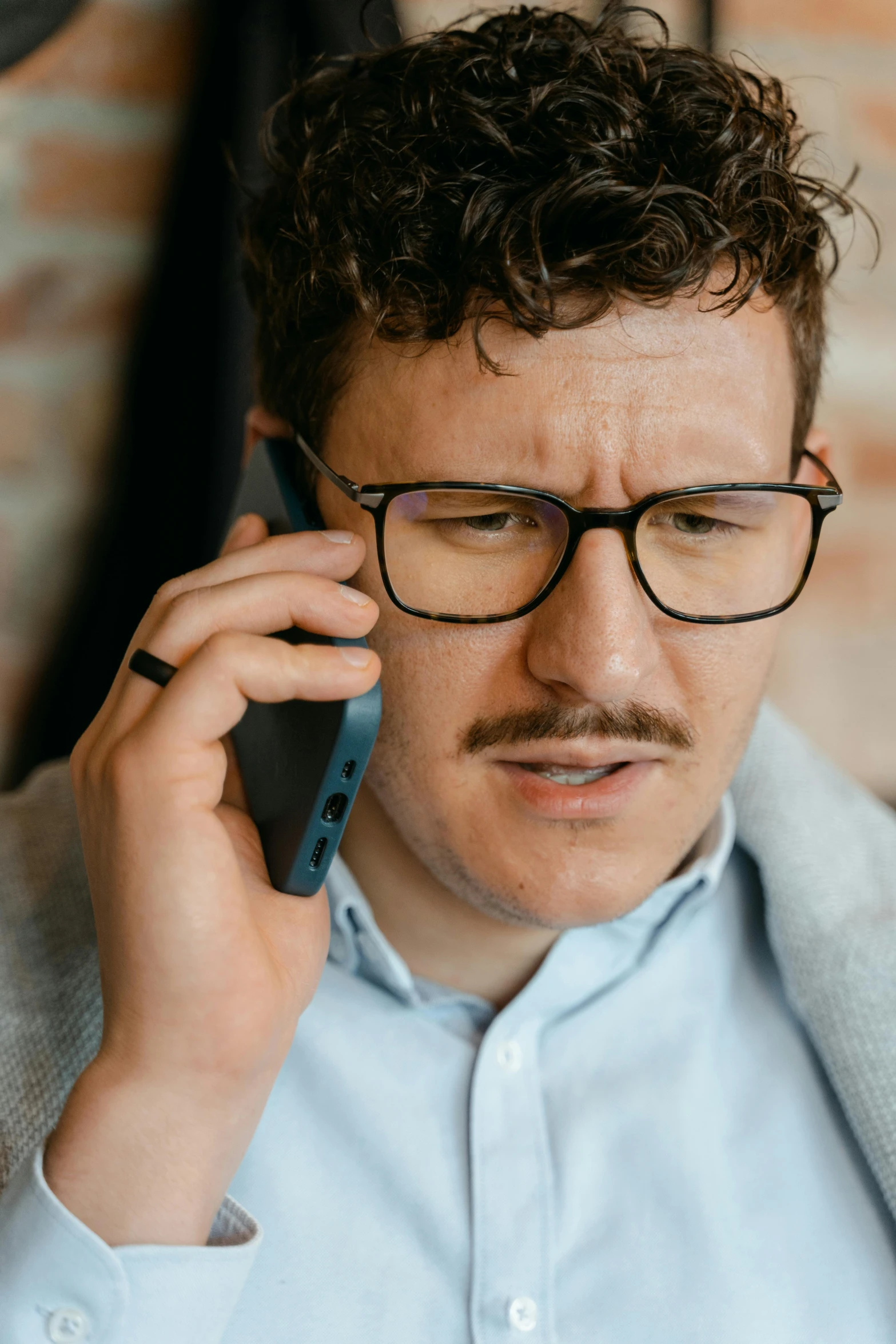 a man with glasses talking on a cell phone, non-binary, scruffy man, selling insurance, thin moustache
