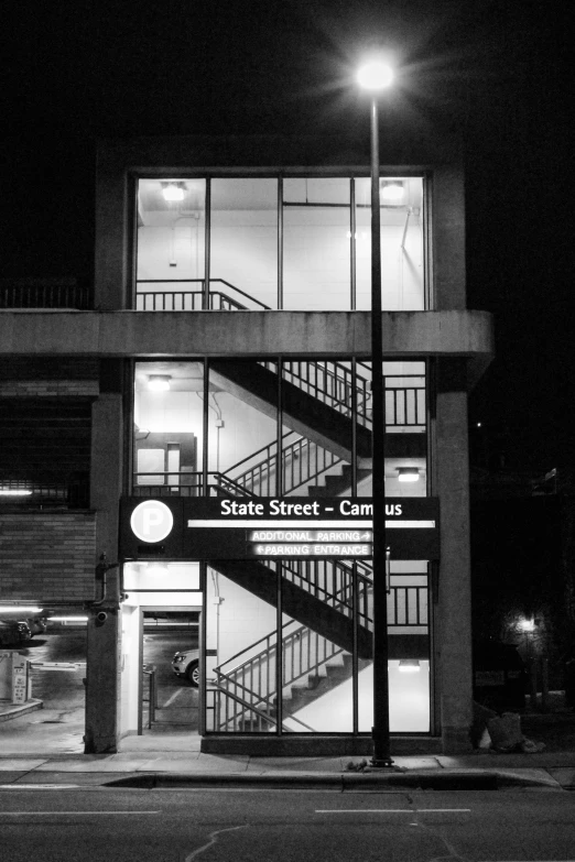 a black and white photo of a building at night, inspired by Thomas Struth, brutalism, platform 9 3 / 4, penrose stairs, bus stop, color contrast