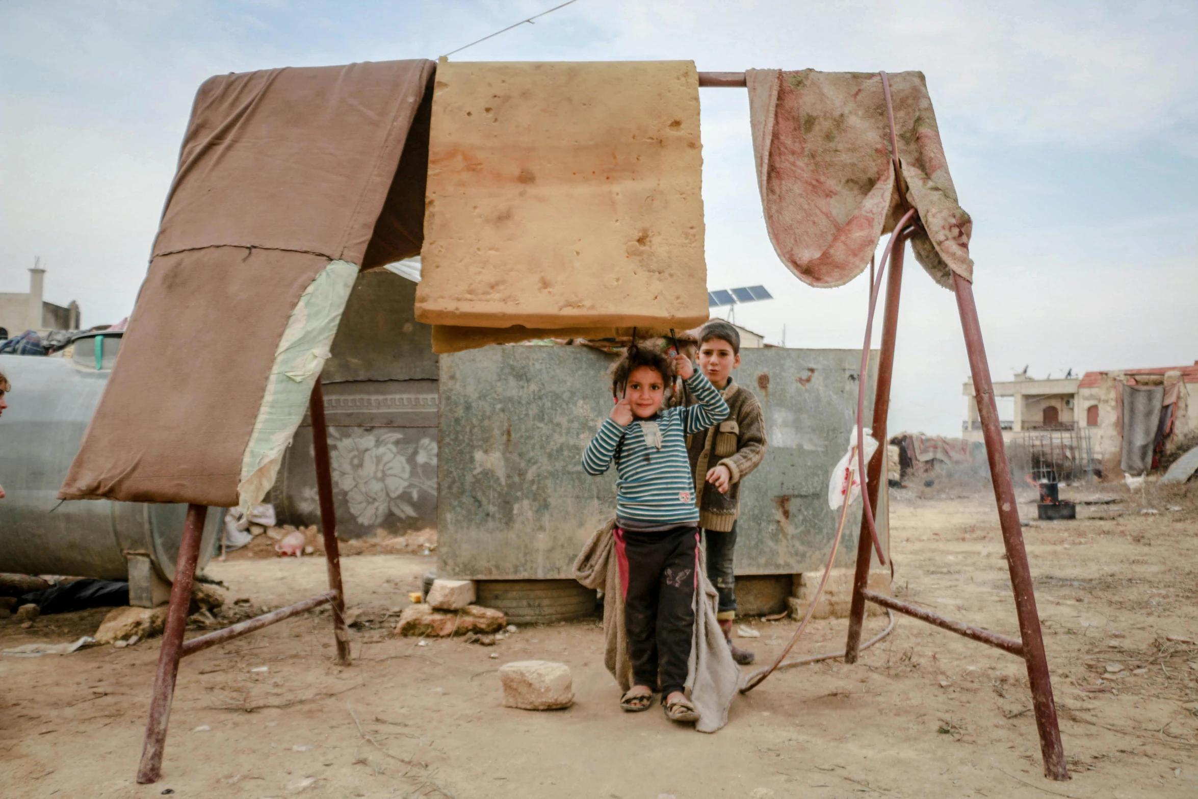 a couple of kids that are standing in the dirt, by Nathalie Rattner, trending on unsplash, arte povera, makeshift houses, sukkot, concrete housing, 15081959 21121991 01012000 4k