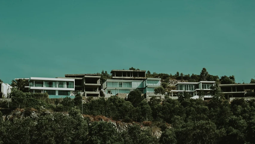 a house sitting on top of a lush green hillside, unsplash contest winner, brutalism, white houses, teal aesthetic, grey, resort
