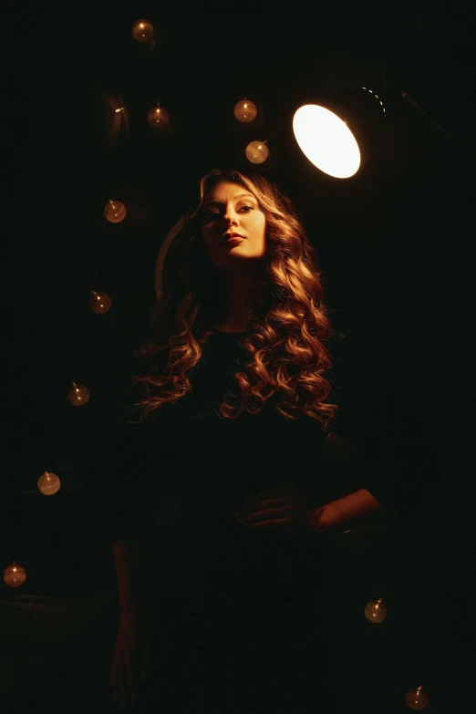 a woman standing under a light in the dark, an album cover, unsplash, renaissance, long wavy brown hair, holiday season, film noir lighting, indoor picture