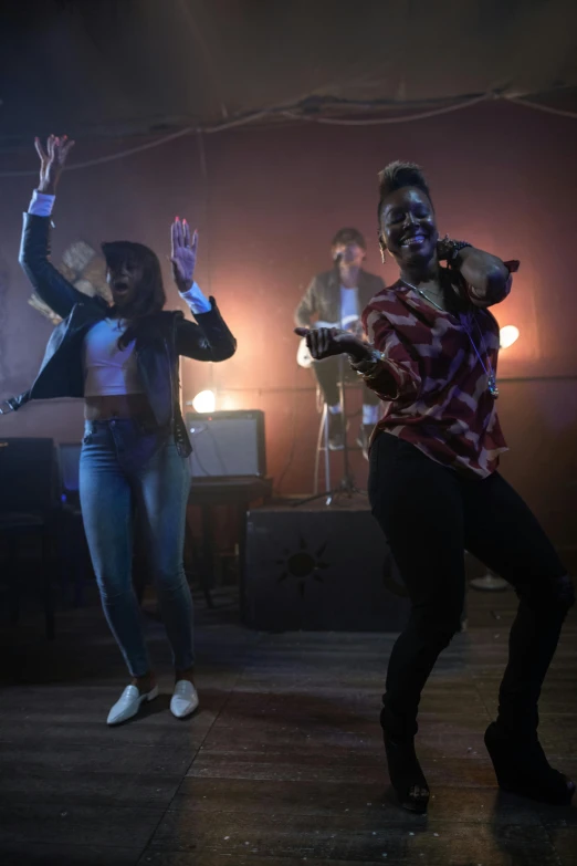 a group of people standing on top of a wooden floor, other women dancing behind, bisexual lighting, medium shot of two characters, maria borges