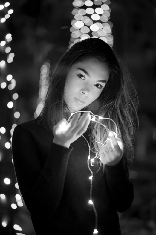 a woman holding a string of lights in her hands, a black and white photo, by irakli nadar, soft devil queen madison beer, anna nikonova aka newmilky, a young asian woman, black an white