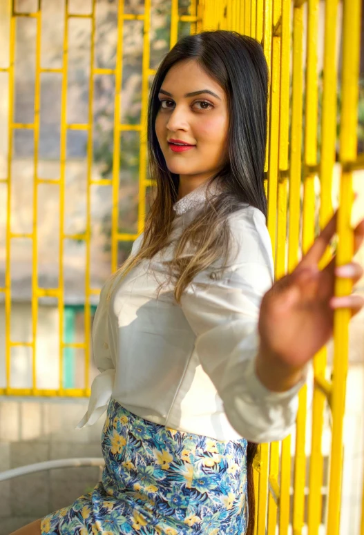 a woman posing for a picture in front of a yellow fence, a picture, by Max Dauthendey, pexels contest winner, wearing a white blouse, young himalayan woman, trending on artstion, wearing an elegant outfit