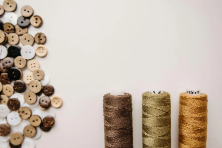 three spools of thread next to a pile of buttons, trending on pexels, brown robes, 9 9 designs, brown, industries