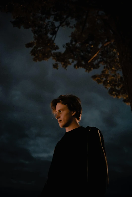 a man standing under a tree at night, an album cover, unsplash contest winner, realism, portrait of tom holland, angle profile portrait, taken in the late 2010s, skydsgaard