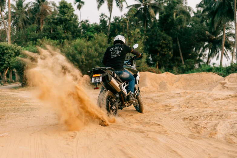 a person riding a motorcycle on a dirt road, covered in sand, as well as scratches, jungles in the background, curvy build