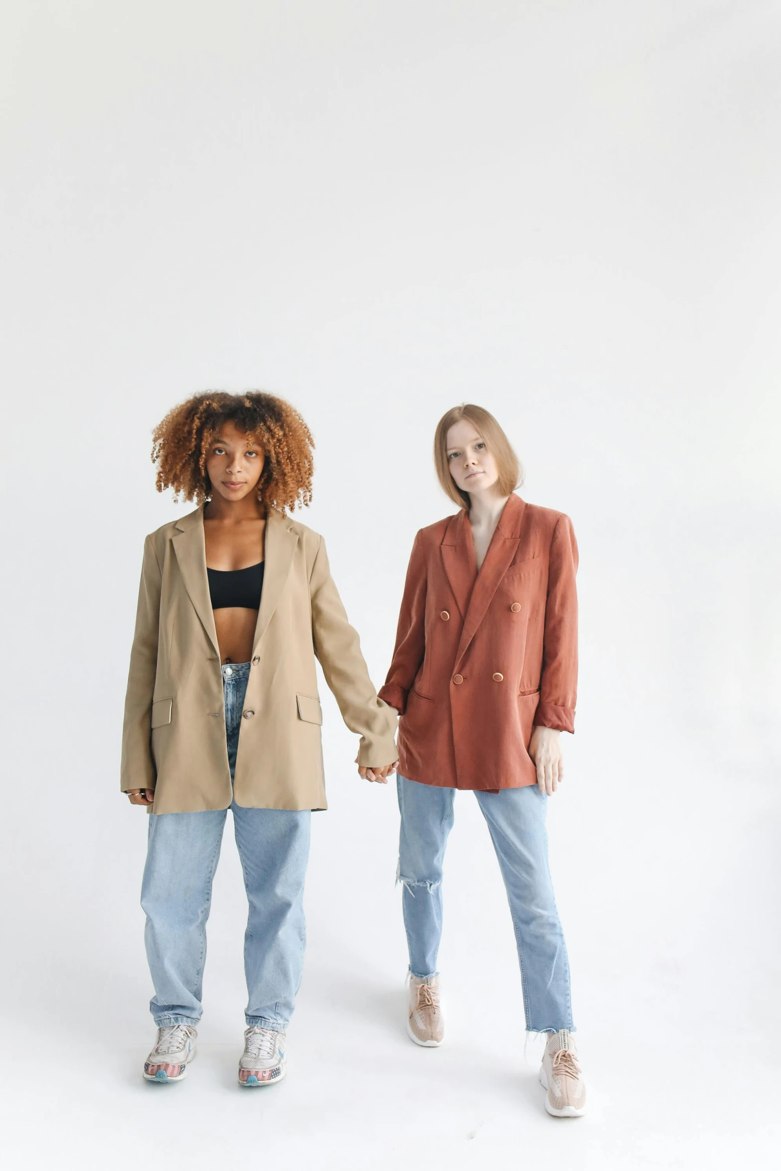 two women standing next to each other holding hands, by Nina Hamnett, trending on pexels, renaissance, wearing a blazer, bleached, teenagers, plain background