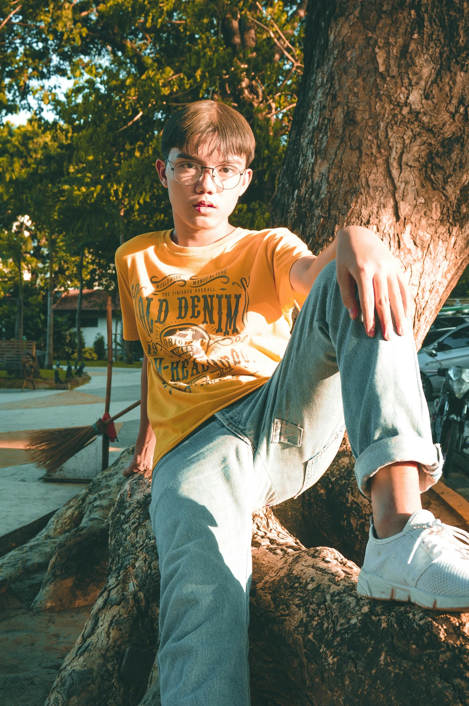 a young man sitting on top of a tree, by Robbie Trevino, trending on pexels, photorealism, wearing a modern yellow tshirt, non binary model, with glasses, style of stranger things