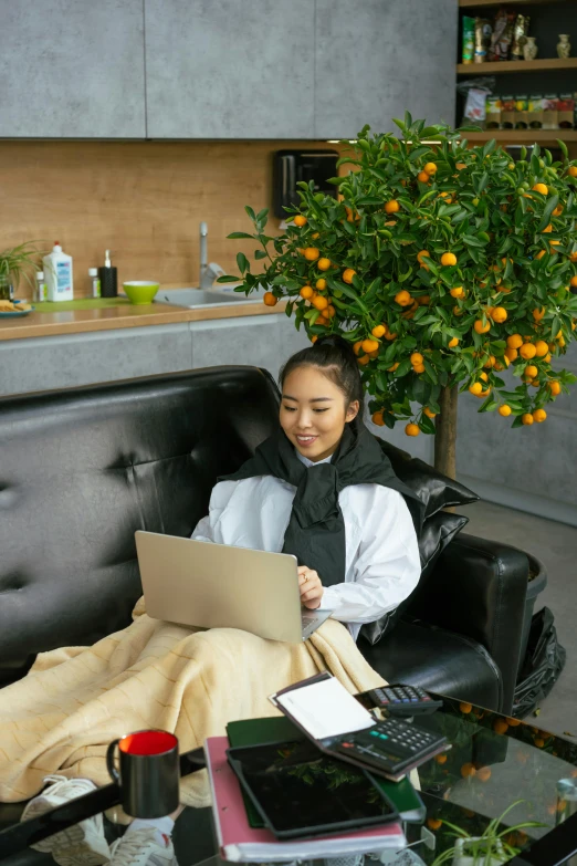 a woman sitting on a couch using a laptop, by Yang J, happening, wearing nanotech honeycomb robe, an orange, vietnamese woman, seasonal