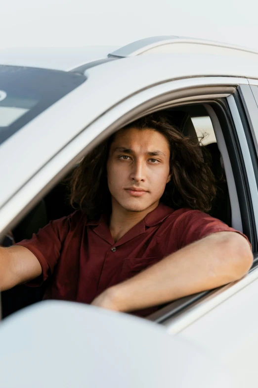 a man sitting in the driver's seat of a white car, renaissance, with long curly hair, non binary model, native american, square