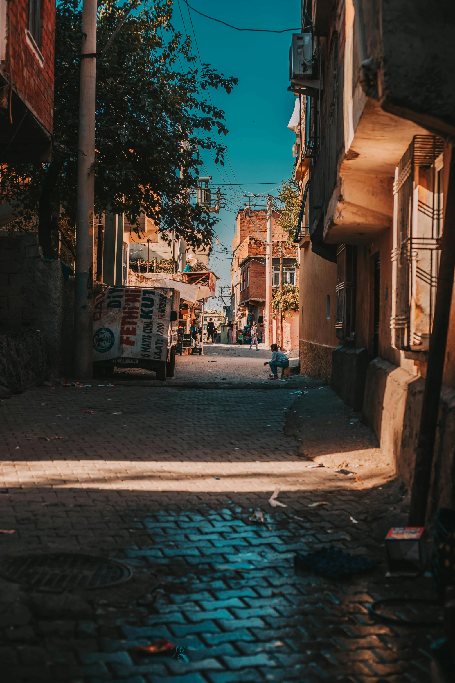 a narrow cobblestone street in an old town, pexels contest winner, happening, fallout style istanbul, late afternoon sun, in the middle of a small colony, belongings strewn about