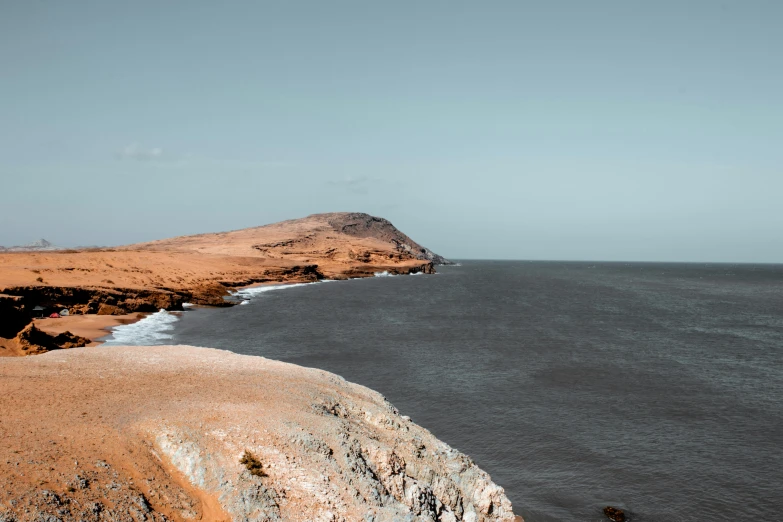 a large body of water sitting on top of a sandy beach, a colorized photo, pexels contest winner, les nabis, on a cliff, oman, silver and muted colors, nazare (portugal)