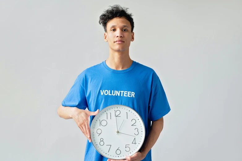 a man in a blue shirt holding a clock, wearing a t-shirt, 2022 photograph, diverse, thumbnail