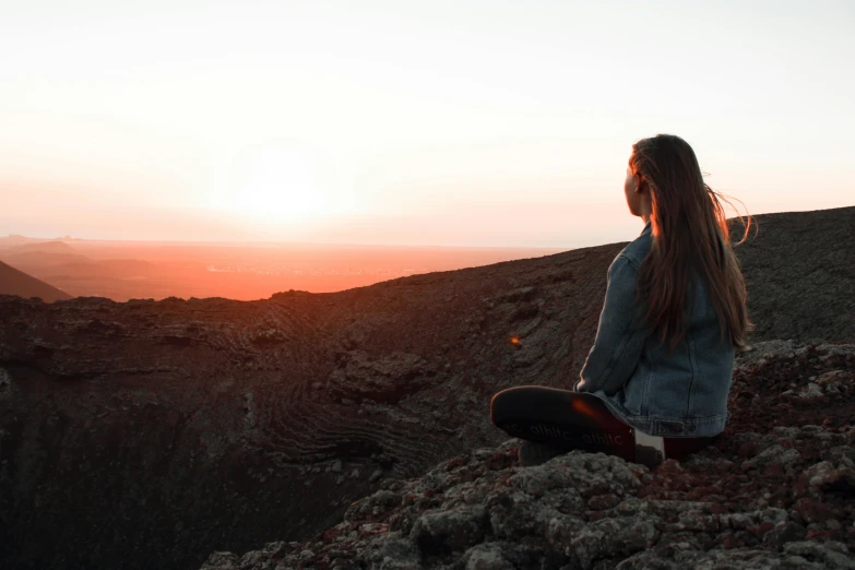 a woman sitting on top of a mountain at sunset, pexels contest winner, happening, meditation, in a volcano, distant expression, sitting down casually