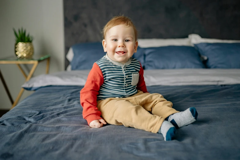 a little boy that is sitting on a bed, inspired by Bedwyr Williams, pexels contest winner, red and blue garments, small smile, 15081959 21121991 01012000 4k, bowater charlie and brom gerald