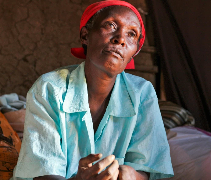 a woman sitting on a bed in a room, hurufiyya, unmistakably kenyan, concerned, older woman, looking serious