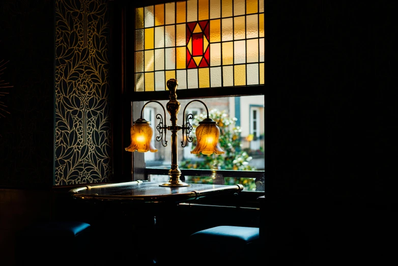 a lamp sitting on top of a table next to a window, inspired by Richmond Barthé, unsplash, art nouveau, sitting at the bar, victorian era, looking around a corner, golden dappled lighting