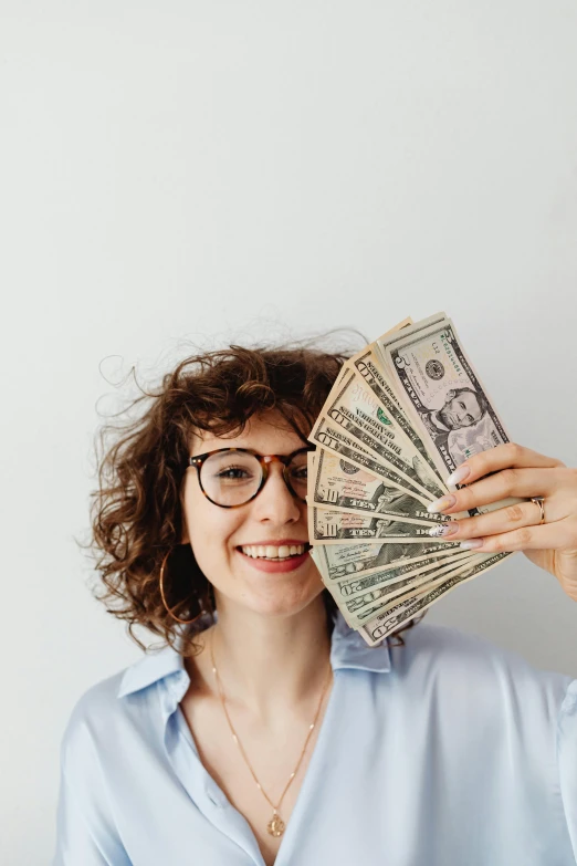 a woman holding a stack of money in front of her face, a portrait, pexels contest winner, renaissance, curly bangs, set against a white background, smiling young woman, 🚀🌈🤩