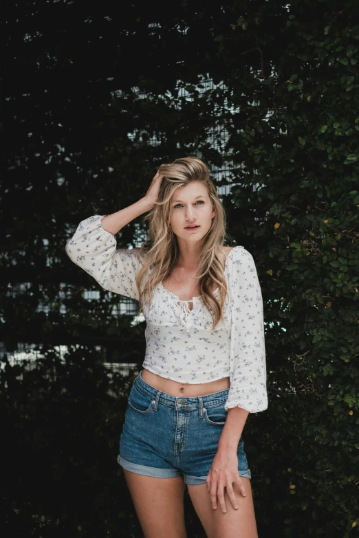 a woman standing in front of a tree, an album cover, inspired by Beatrice Huntington, unsplash, renaissance, crop top, portrait of kim wexler, wearing jeans, floral clothes