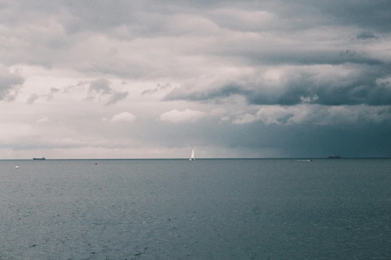 a group of boats floating on top of a large body of water, unsplash contest winner, minimalism, ominous clouds, shaped like a yacht, lone person in the distance, seaview