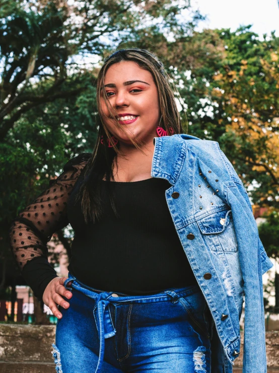 a woman standing in front of a fire hydrant, an album cover, by Olivia Peguero, pexels contest winner, happening, wearing a jeans jackets, she has a jiggly fat round belly, smiling and looking directly, patterned clothing