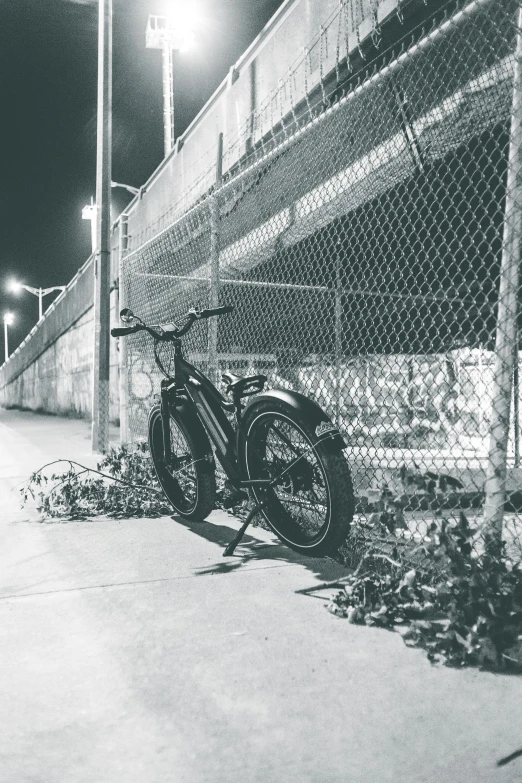 a black and white photo of a bike leaning against a fence, illuminated, electric, steel gray body, urban patrol