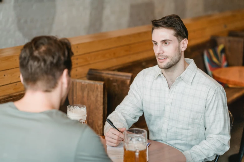 a man sitting at a table with a glass of beer, facing each other, lachlan bailey, customers, casually dressed