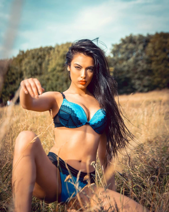 a woman in a blue bikini sitting in a field, inspired by Elsa Bleda, unsplash, posing ready for a fight, very sexy woman with black hair, 2019 trending photo, 5 0 0 px models